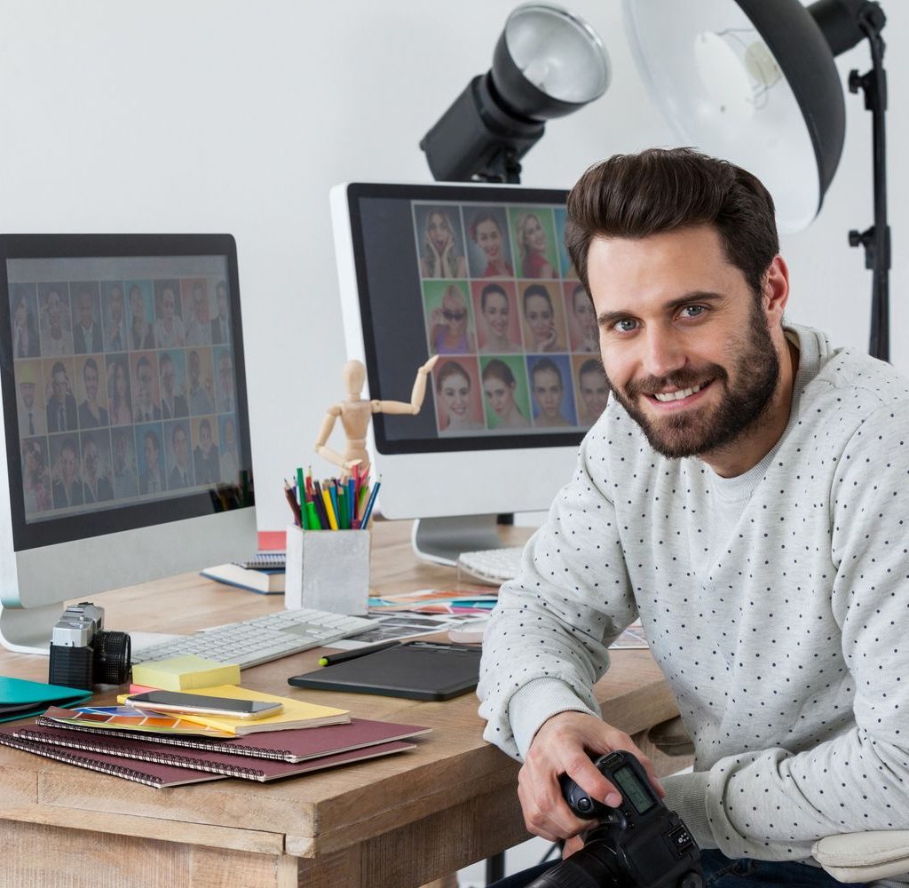 Happy Photographer Holding Camera At His Desk 9REYFMZ 1024x1000
